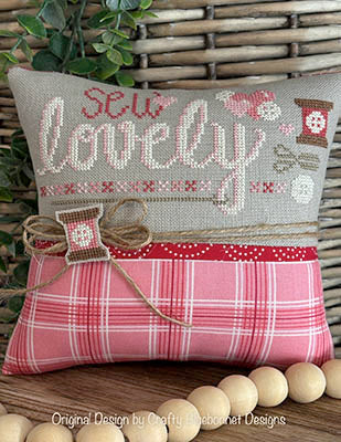 Valentine-themed cross stitch pattern with the word “Lovely” stitched in soft colors, finished as a small pillow, by Crafty Bluebonnet Designs.