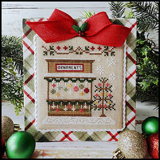 Ornament Stand cross stitch pattern by Country Cottage Needleworks featuring a wooden market stall with hanging Christmas ornaments, greenery garland, and a decorated tree in a festive winter scene