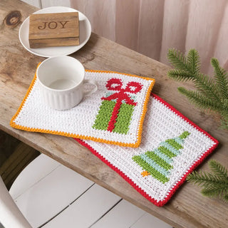 Two crocheted placemats with Christmas designs on a wooden table.