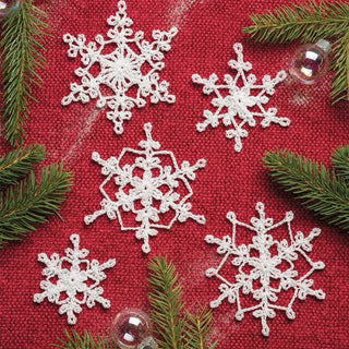 White crocheted snowflakes on a red fabric background with green pine branches.