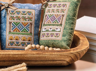 Two cross-stitched pillows with intricate patterns in a wooden bowl.