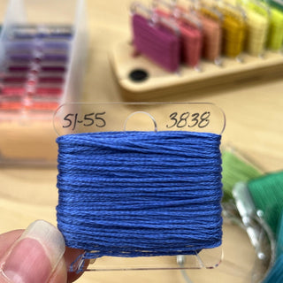 Blue thread spool with a label held by a hand, with sewing supplies in the background.