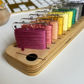 Wooden thread holder with colorful spools of thread on a white surface.