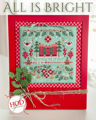 Cross-stitch design featuring two red houses, trees, birds, ornaments, and holiday florals stitched on aqua fabric, finished in a red frame with gingham backing and twine accent.