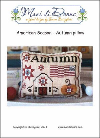 Cross stitch pattern pillow with an autumn theme, featuring a barn and pumpkins on a beige background, labeled 'American Season - Autumn Pillow' by Mani di Donna.