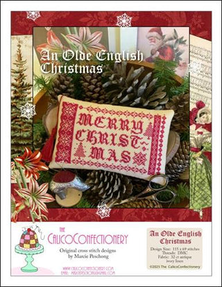 Red monochromatic cross-stitch design reading “Merry Christmas,” bordered with traditional sampler motifs, small trees, a star, and decorative banding, finished as a rectangular pillow displayed with pinecones and Christmas décor.