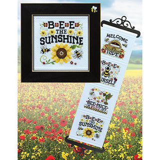 Decorative cross-stitch kit with bee-themed designs against a field of flowers.