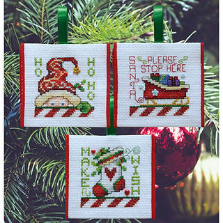 Cross-stitched Christmas-themed cards on a green leafy background