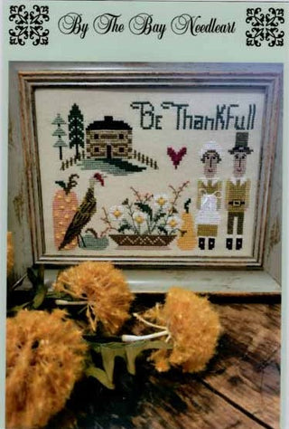 Cross-stitch design featuring pilgrims, pumpkins, a turkey, cornucopia, fall flowers, and the phrase ‘Be Thankful,’ stitched in warm autumn colors in a folk-art style by By The Bay Needleart.