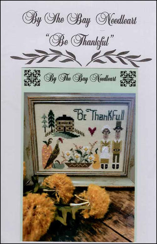 Cross-stitch design featuring pilgrims, pumpkins, a turkey, cornucopia, fall flowers, and the phrase ‘Be Thankful,’ stitched in warm autumn colors in a folk-art style by By The Bay Needleart.