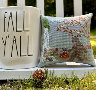 Bigfoot in Fall Cross Stitched pillow with accompanying decoration in an  outdoor setting.