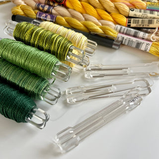Colorful embroidery threads on acrylic bobbin pegs with visible labels on a white background