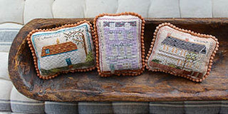 Three cross stitched pillows on a wooden tray against a neutral background