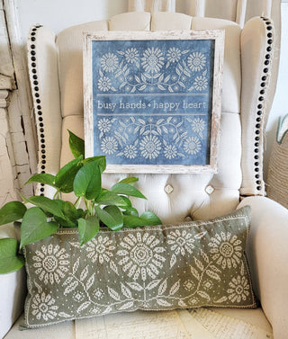 Decorative pillow with floral pattern on a chair with a framed print above it.