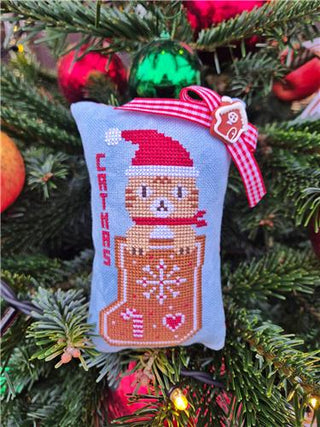 Cross-stitched ornament of a bear in a boot with a gingerbread man hat on a Christmas tree.
