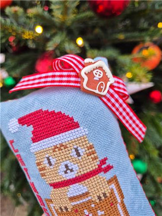 Cross-stitched gingerbread man ornament with a red bow on a Christmas tree background