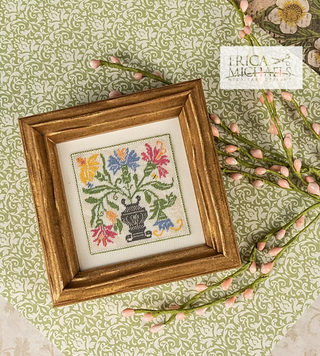 Framed cross-stitched floral design on a decorative background with 'Erica Michaels' branding.
