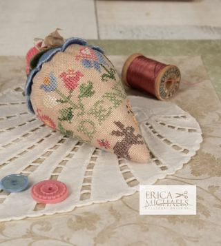 Decorative fabric heart with floral patterns on a lace doily, accompanied by a spool of thread and buttons.
