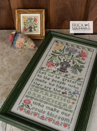 Framed cross-stitched piece with floral design and text, placed on a wooden surface.
