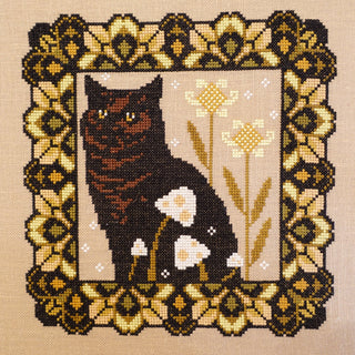 Cross-stitched design of a brown & black cat with flowers in a decorative frame.