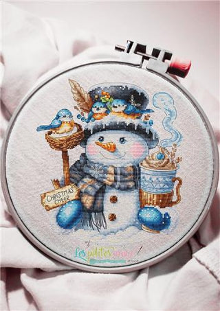 Cross-stitched snowman design with birds and a mug of hot chocolate in an embroidery hoop.