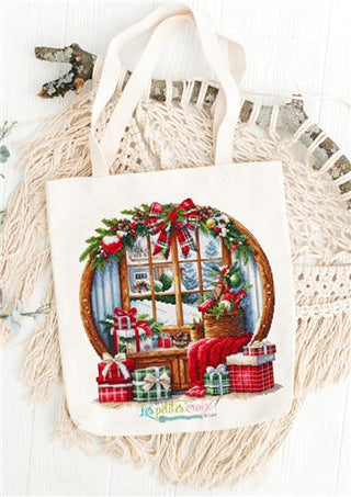 Tote bag with Christmas design featuring a window and presents, placed on a textured surface.