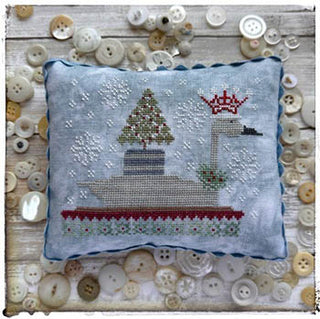 Stitch a whimsical winter scene with Christmas Swan by Lucy Beam. This counted cross stitch pattern features a crowned swan carrying a Christmas tree amid falling snow, finished as a charming holiday pillow.
