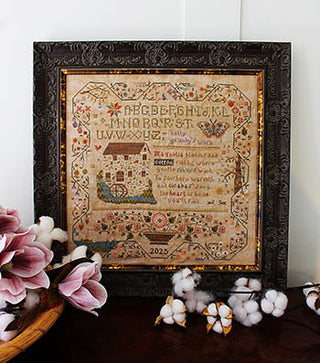 Decorative framed cross stitched piece with floral and cotton decorations on a white wall.