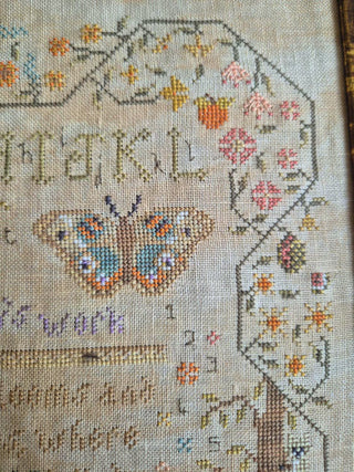 Cross-stitched butterfly design with floral elements and text on fabric