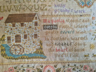 Close-up of a cross-stitched piece with a house, text, and floral patterns.