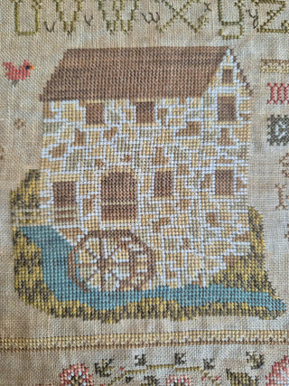 Cross-stitched design of a water mill on fabric