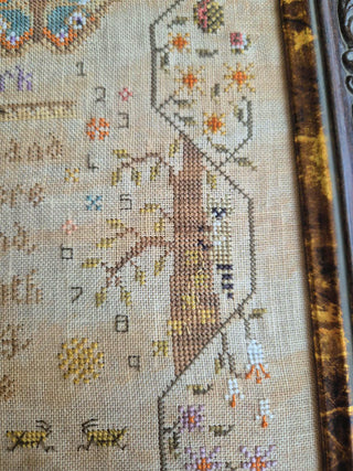 Close-up of a cross-stitched piece with floral patterns and text on fabric.