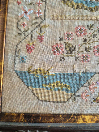 Close-up of a detailed cross-stitched piece with floral patterns and a bowl.