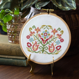 Embroidery hoop with floral pattern on a stand, surrounded by books and plants.