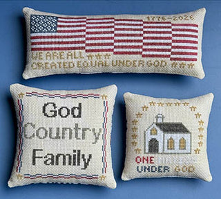 Three patriotic cross stitch pillow designs featuring American flag motifs and phrases including “God Country Family” and “One Nation Under God” on neutral fabric backgrounds.