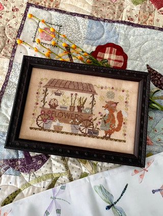 Framed cross-stitched piece with a fox and garden scene on a quilt background