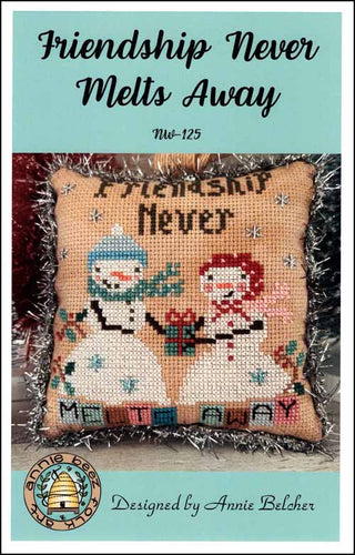 Cross-stitched pillow with snowmen design and text 'Friendship Never Melts Away' on a teal background.