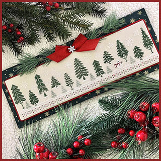 Cross-stitched winter design featuring a long row of green evergreen trees with falling snow and a pair of red skis, finished in a rectangular display with holiday greenery.