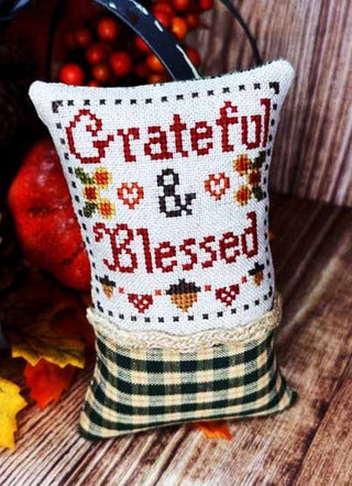 Decorative pillow with 'Grateful & Blessed' text on a wooden surface with autumn decorations.