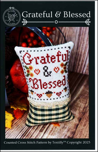 Cross-stitched pillow with 'Grateful & Blessed' text on a wooden surface with pumpkins and leaves.
