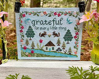 Cross-stitch design featuring the phrase “grateful for every little thing” surrounded by birds, squirrels, florals, and nature motifs within a scalloped floral border.