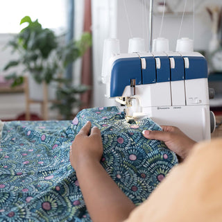 Person using a sewing machine on floral fabric with a blurred indoor background