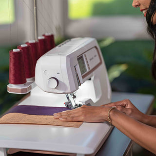 Person using a sewing machine with red thread spools on a blurred background