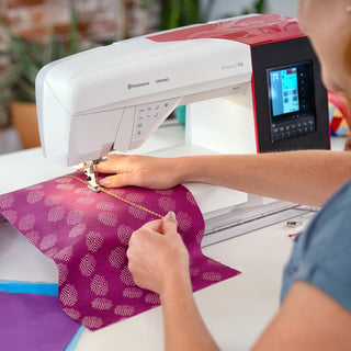 Person using a sewing machine on a piece of purple fabric with a pattern.
