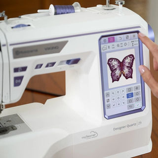 Sewing machine with digital display showing a butterfly design, being operated by a hand.
