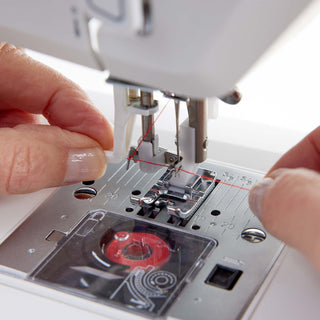Close-up of a sewing machine with a hand threading the needle.