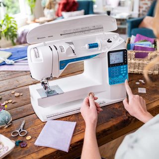 Person using a sewing machine on a wooden table with various sewing materials.
