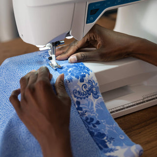 Person using a sewing machine on blue fabric with white patterns