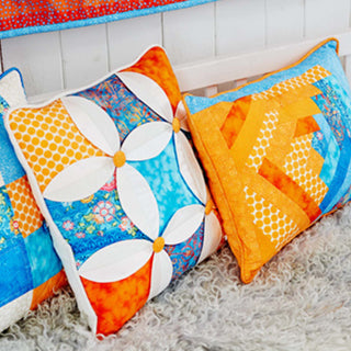 Colorful quilted pillows with floral and geometric patterns on a textured surface.