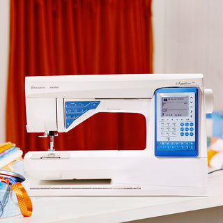 White sewing machine with digital display on a table against a red curtain background